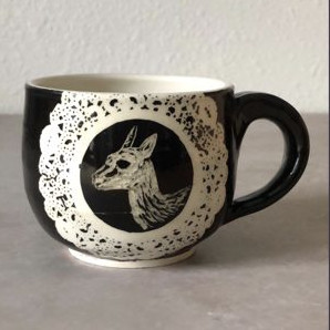 Black mug with lace medallion framing a llama illustration
