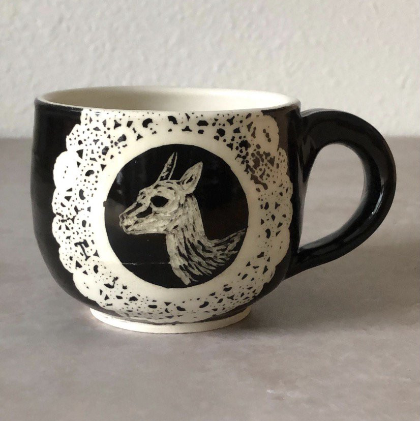 Black mug with lace medallion framing a llama illustration